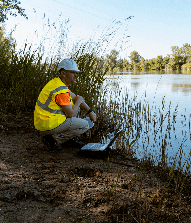 Worker with laptop by a lakeside.