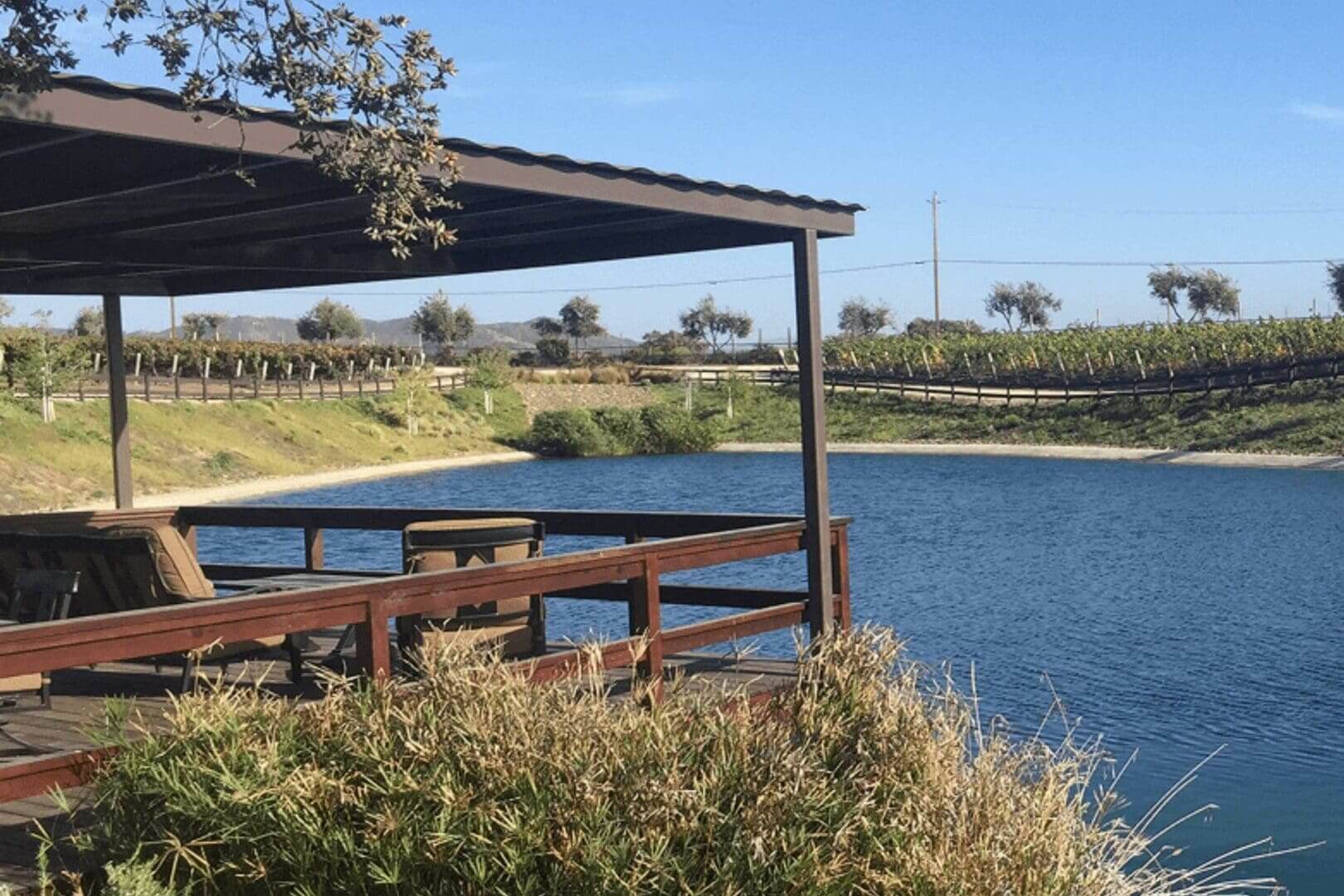 Wooden picnic tables under a shaded pavilion by a calm lake.